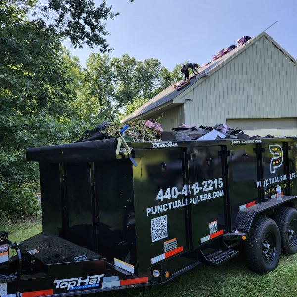 dumpster filled with roofing material and roofers working in background